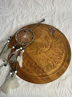 Photo showing all three items in the lot: wooden circular wall hanging with engraved indigenous design, dreamcatcher with feathers and beads, and a pair of copper dangle earrings.