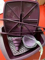 Photo showing large purple silicone microwave steamer multi-cooker with perforated tray inside, accompanied by purple silicone tongs, collapsible funnel and bundle of silicone baking cups.
