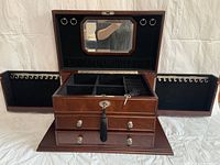 Jewelry box open showing compartments, ring holders on side doors, octagonal mirror on lid, and key with tassel in lock