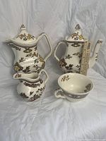 Four-piece set of Mason's Manchu Brown vintage ironstone: two teapots, a creamer, and a teacup with saucer, showing front detail and floral patterns.