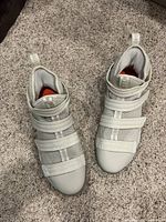 Top-down view of pair of light grey Nike Zoom athletic shoes with velcro straps on carpeted surface.