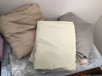 Folded queen size sheets in beige, off-white, and gray colors stacked on transparent plastic bin