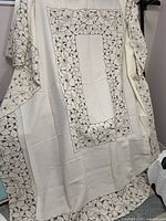 Full view of vintage cream tablecloth showing coffee coloured floral cutwork embroidery along edges and central rectangle pattern, draped vertically.