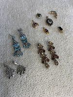 Full lot photo showing various pendants and earrings with blue, red, green, black and purple stones in silver and gold tone metals on a fabric background