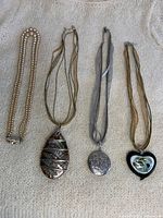 Overview of four necklaces including a pearl bead necklace, two glass corded pendant necklaces, and a silver locket pendant necklace.