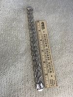 Sterling silver bracelet measured against a ruler showing approx 7.5 inches length, placed on a textured beige fabric.