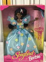 Front view of the boxed 1995 Mattel Songbird Barbie doll dressed in blue gown with floral accents, showing the doll and bird accessory through the clear plastic window.