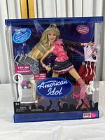 Front view of the Barbie American Idol Edition doll packaging showing the doll in pink and black outfit, karaoke machine, microphone stand, additional outfit and boots.
