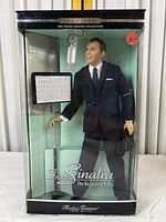 Front view of the Frank Sinatra doll inside original box showing the doll in a suit, microphone, and music stand.
