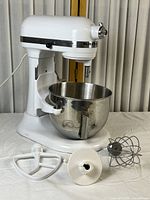 Front three-quarter view of white mixer on table with bowl and attachments laid out