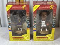 Photo showing two boxed Headliners basketball figurines of Shaquille O'Neal and Scottie Pippen side by side, visible through window packaging with bright yellow and red box art and crowd backdrop.