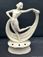 Front view of the off-white ceramic dancer flower frog showing the elongated arms and looped drape behind.