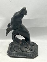 Front angled view of black cast metal sea lion bookend with geometric base and stylized waves.