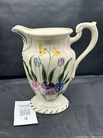 Ceramic pitcher with hand-painted floral design in tulip and daffodil motifs and black trim accents.