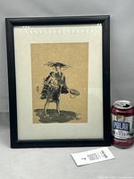 Framed artwork next to can for scale, showing full artwork inside black frame under glass.