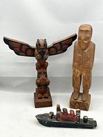 Three carved wooden objects: Northwest Coast-style totem with eagle and bear, folk art male figure, and painted toy steamship; all displayed against a plain background.