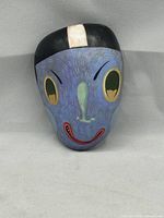 Front view of the hand-painted rock showing the cartoon-like face in purple, green, yellow, and red colors.