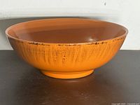 Side view of the orange ceramic bowl showing drip pattern and rim accents.