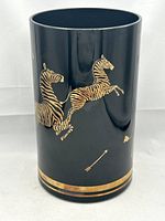Front side showing two gold zebras in mid-leap with an arrow below and gold bands on base rim.