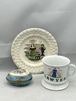 Photo of three decorative porcelain collectibles: Georgian child's plate with daisy border and transfer scene, vintage lawyer shaving mug, and hand-painted blue Limoges porcelain egg trinket box.