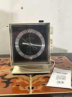 Front view of the vintage General Electric clock radio with black dial and silver markings, set on decorative tile surface.