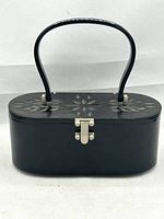Front view of vintage black lucite handbag with carved floral design and metal clasp.