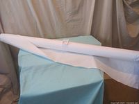 Photo showing a bolt of white 100% cotton fabric still attached on the roll placed on a blue surface with a paper label number 119