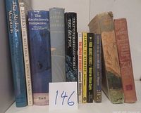 Front row of eleven books standing upright on a shelf showing spines and dust jackets.