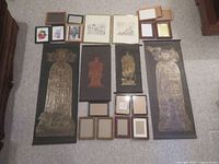 Top-down view of brass rubbings, several small framed prints and multiple small empty picture frames arranged on carpet floor.