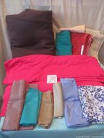 Assorted folded fabrics of various solid colors including dark brown, turquoise, red, pink, beige, lavender, with a bright pink fabric piece laid out in the center