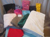 Photo of assorted fabrics including a large roll of white corduroy, plus several folded pieces in various colors and materials