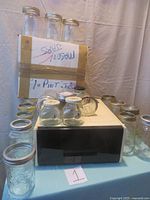 Multiple clear glass canning jars with metal lids, some small and some 1-pint size, arranged on and around a white box.