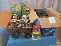Box of metal canning lids and rings along with boxed Certo pectin and Parowax sealing wax on a blue tablecloth.