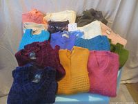 Top view of assorted knit sweaters in various colors including pink, white, blue, maroon, yellow, green