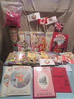 Overall view of all items in the lot, showing Rupert Annuals, Sta-Lox tube with bricks, flags, party games booklets, and pop-up book