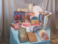 Full view of the sewing and knitting book collection displayed on a table, also showing a box containing patterns or booklets.