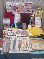Overall assortment of sewing patterns displayed with multiple fabric pieces in various colors including red, white, maroon, yellow, blue, and beige.