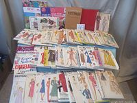 Full lot on display showing many envelopes of sewing patterns, some books, and craft guides related to sewing and textiles.