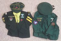 Boy Scout and Cub Scout uniforms laid side by side showing front of garments with badges and caps