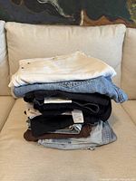 Stack of folded women's pants and jeans, showing variety of colors such as light blue denim, white, black, and tan.