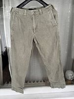 Front view of men's lightweight beige/tan Abercrombie & Fitch jeans hanging on black hanger in natural light, showing overall condition and styling.