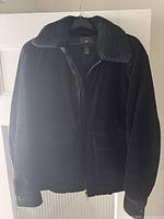 Front view of a black men's corduroy jacket featuring a black faux shearling collar, front zipper, flap pockets and buttoned cuffs.