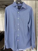 Blue Tommy Hilfiger dress shirt hanging on a hanger, showing front button-down and collar with small white dot pattern.
