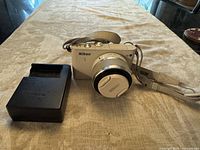 White Nikon 1J3 mirrorless camera with attached 10-30mm lens and Nikon camera strap, placed on light table surface.