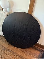 Top view of round black dining table showing wood grain and some surface wear.