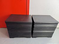 Set of two black wooden nightstands shown side-by-side with visible drawer design and base detail.