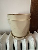 Photo showing two beige plant pots stacked, with wave patterns and matching saucers underneath.