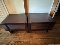 Two heavy, block-style wooden nightstands with dark finish placed side by side, showing top and front sides.