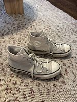 Side view of the cream suede Converse high-top sneakers showing profile, laces, logo patch, and platform sole on carpet.