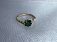 Front angled view of the 14k gold ring with green stone on a white textured surface, showing prong setting and swirl design.